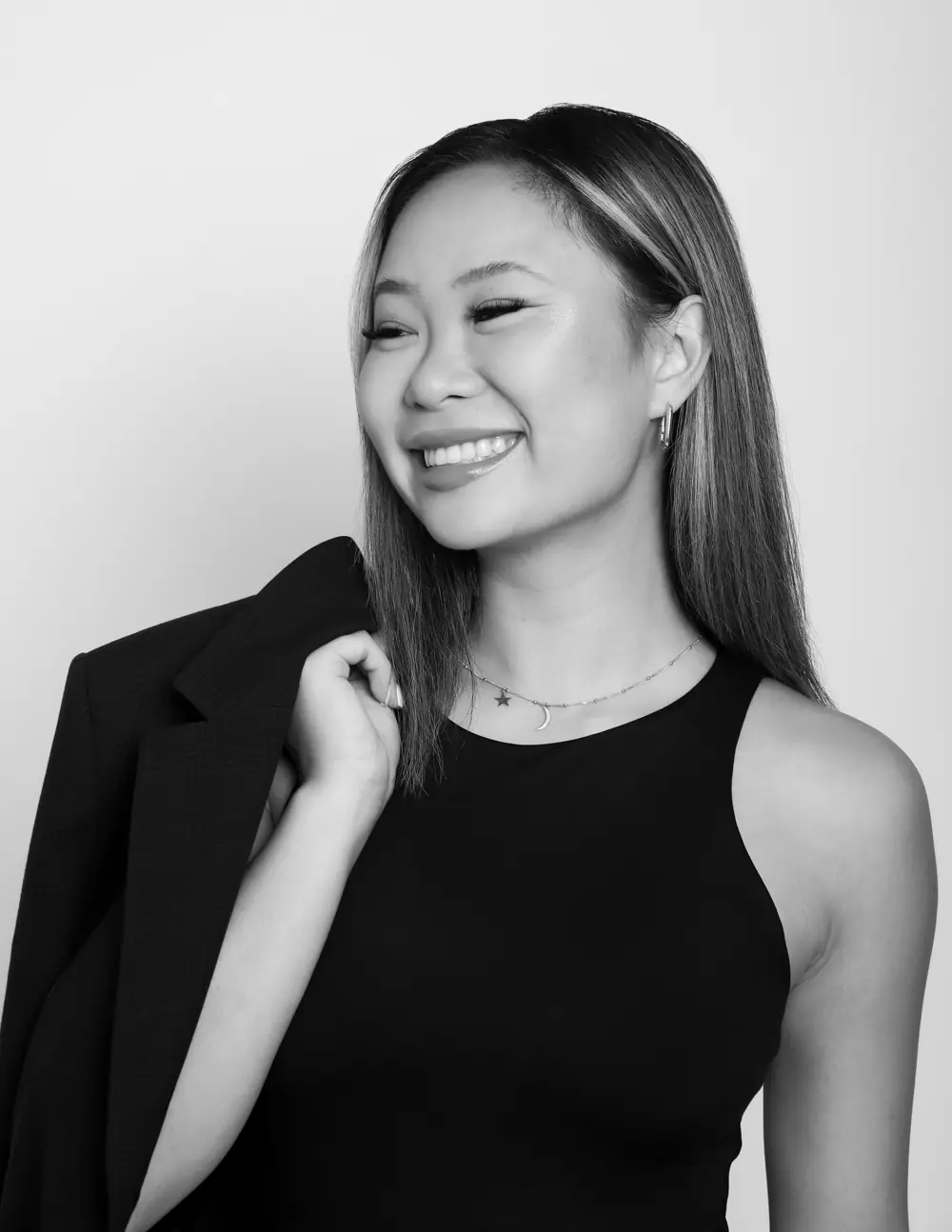 Black and white portrait of Lizzie smiling, a blazer over her shoulder.