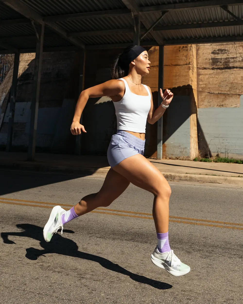 Lizzie mid-stride on a sunlit street, running in a white tank and lavender shorts.